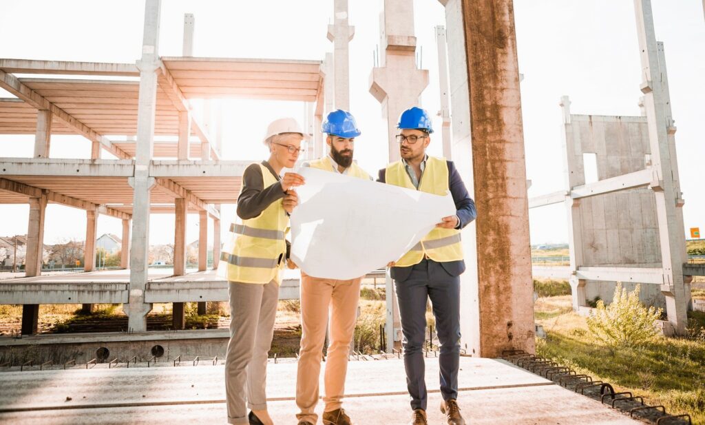Une femme et deux hommes analysent des plans sur un chantier – Exemple de coordination technique et suivi opérationnel sur le terrain